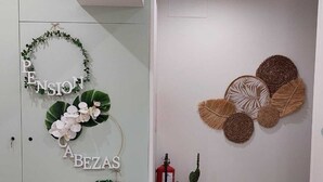 Een kamer met een glazen wand waarop in witte letters 'PENSION', 'CA BEZAS' en 'OVIEDO' staan, een cactusplant en een geweven kunstwerk aan de muur.