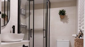 Een moderne badkamer met een douche met glazen wand, een witte wastafel en een toilet.