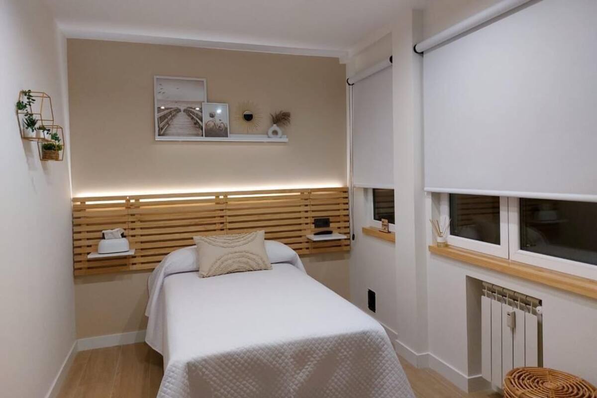 Une chambre à coucher comprenant un lit, une tête de lit dotée d’un éclairage intégré, une fenêtre avec des stores et un radiateur.
