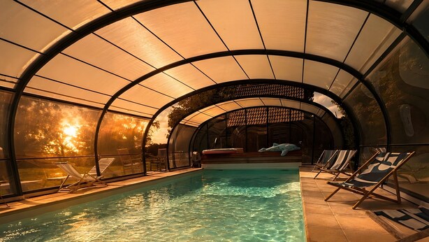 Une piscine intérieure à l’eau claire, entourée de chaises longues et d’un espace abrité doté d’un toit incurvé.