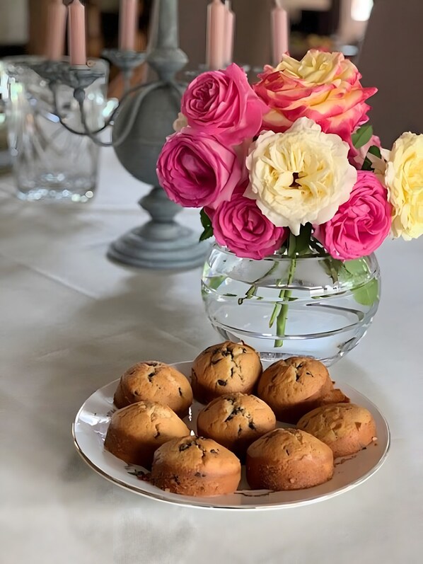 A table with a glass vase of flowers and a plate of muffins.