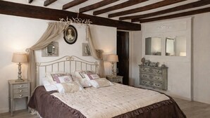 Une chambre à coucher comprenant un lit, deux tables de chevet, une commode, un miroir et un plafond avec des poutres apparentes.