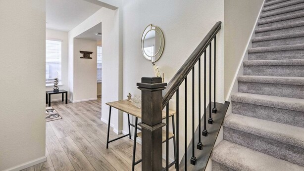 A staircase with a wooden handrail and black balusters, leading to a landing with a round mirror and a small table.