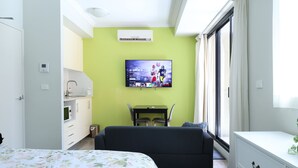A hotel room with a bed, a TV mounted on the wall, a small table with chairs, a window with curtains, and a kitchenette. - Modern Studio + Balcony + Car Park - Darling Harbour (Sydney)