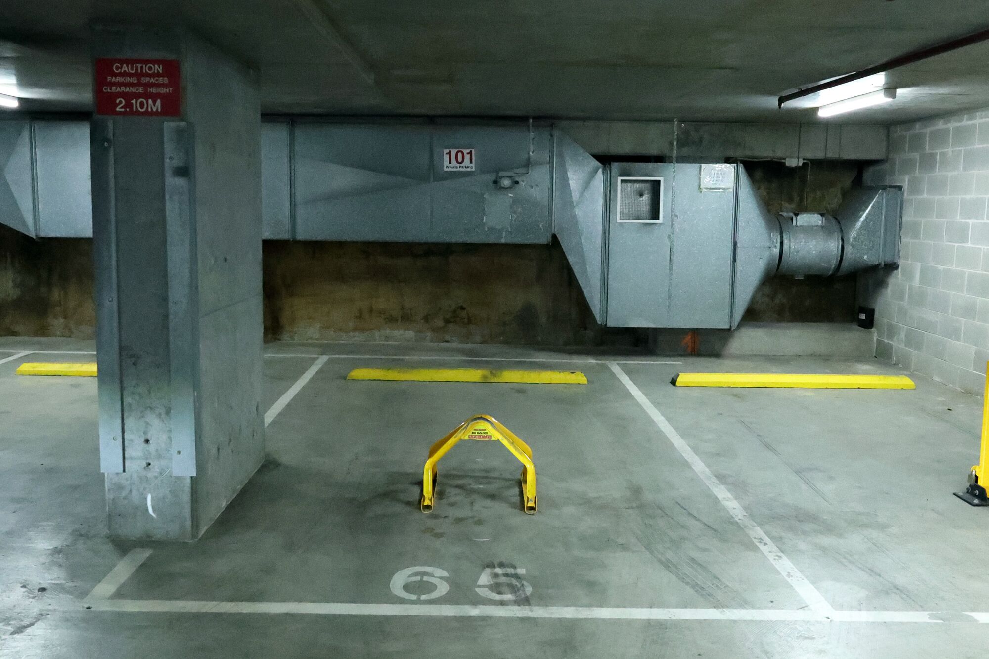An underground parking garage with concrete walls, yellow safety barriers, and a sign indicating a clearance height of 2.10 meters.