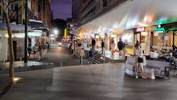 A nighttime street scene with outdoor cafes and shops.