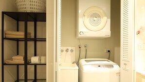 A laundry area with a washing machine, a dryer, and shelves with folded towels and a basket. - Modern Studio + Balcony + Car Park - Darling Harbour (Sydney)