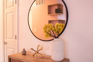 Un espejo en la pared, un jarrón con flores amarillas, y una mesa de madera con un jarrón pequeño y un adorno dorado.
