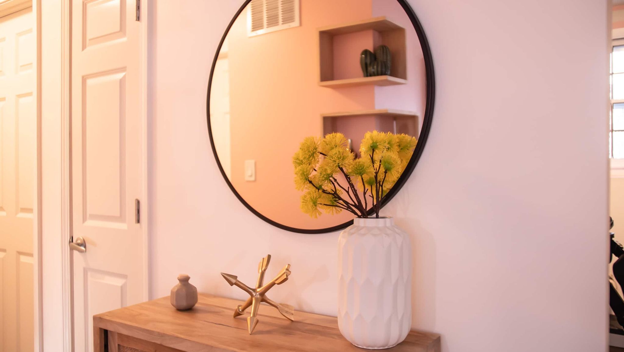 Een spiegel met een bloemstuk van gele bloemen, een vaas en een decoratief object op een houten console.