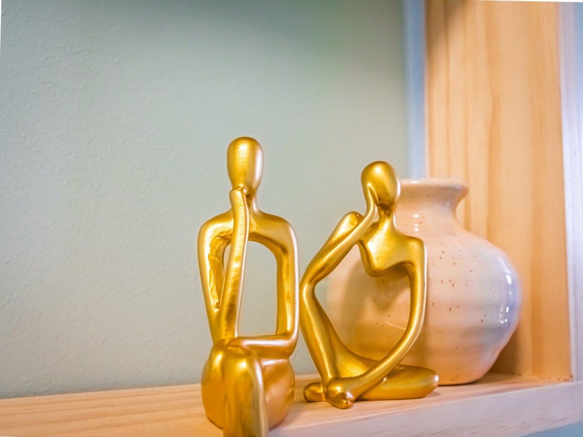 Two golden figurines on a shelf with a white vase in the background.