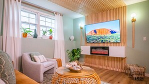 A living room with a flat-screen TV, a sofa, a round wicker coffee table, and a fireplace. - UrbanSerenity: 3Min walk Mass/KU (Lawrence)