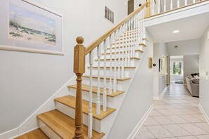 A staircase with wooden steps and white balusters, leading to a landing with a framed artwork of a beach scene. - RBC Heritage Views From Your Deck, 4BR Villa Steps to Harbour Town (Hilton Head Island)