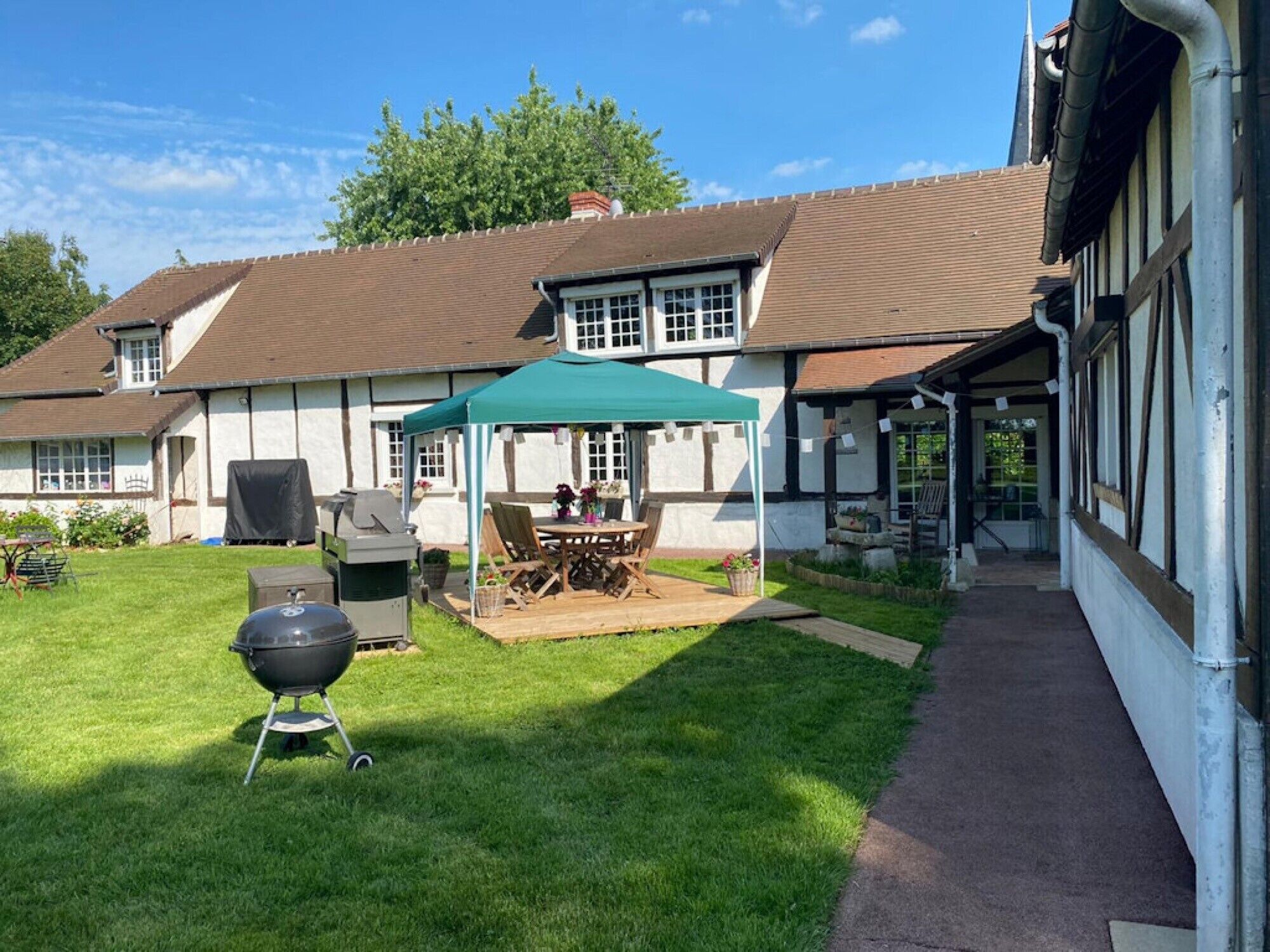 A house with a covered patio, a barbecue grill, and a pathway leading to the entrance.