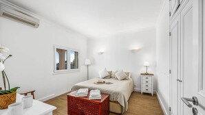 A bedroom with a bed, bedside table, lamp, and a window with a view.