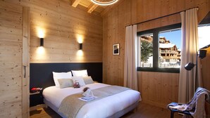 A wooden-paneled bedroom with a bed, bedside lamps, a window with curtains, and a view of a building outside.