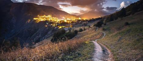 Un valle con un camino que lleva a un pueblo iluminado, situado en las montañas.