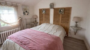 Ein Schlafzimmer mit Bett, Heizkörper, Fenster mit Vorhängen und einer Wandlampe.