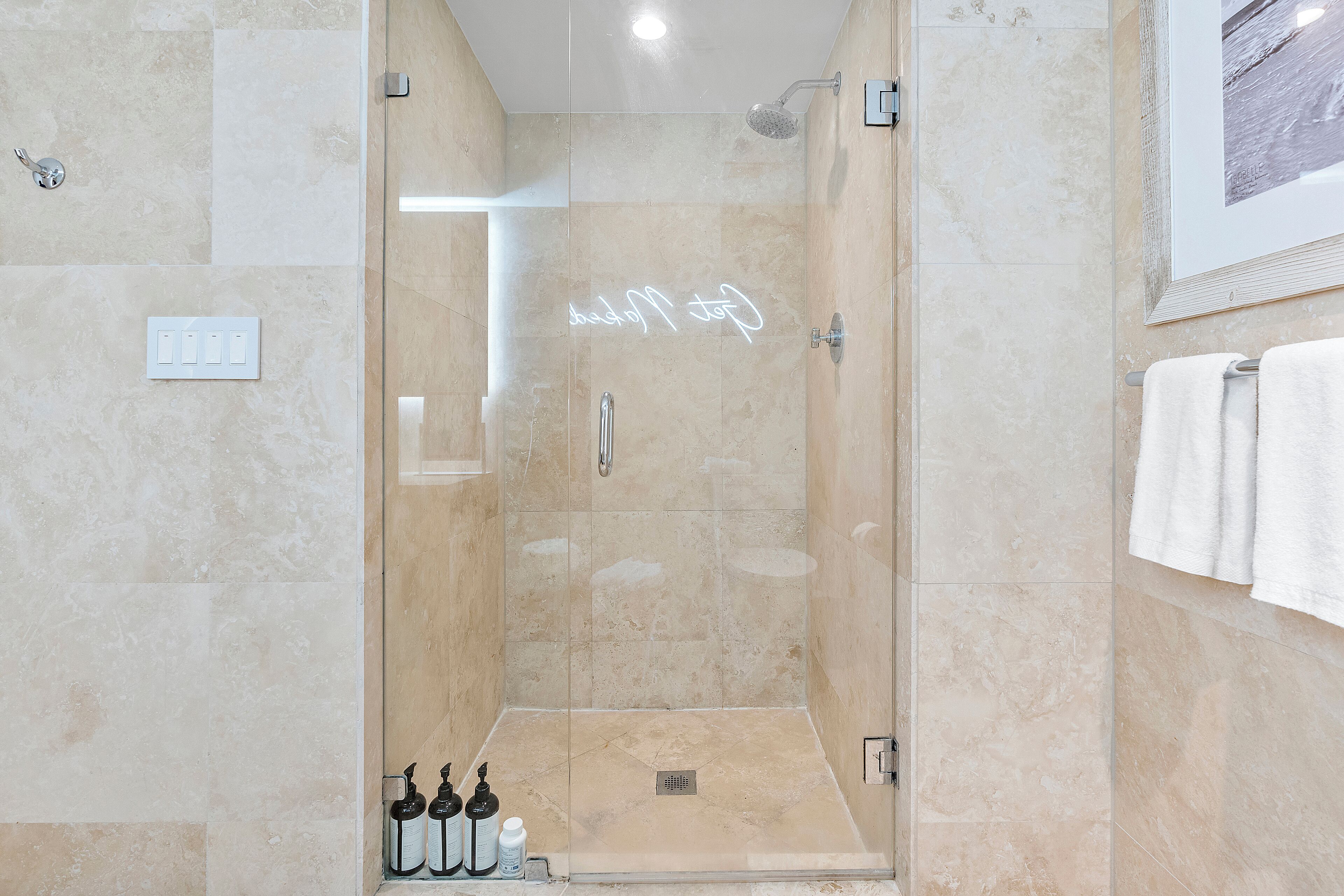 Une douche moderne avec une porte en verre, un porte-serviettes et un tableau encadré au mur.