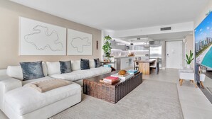Un salon moderne avec un canapé d’angle, une table basse et une cuisine en arrière-plan.