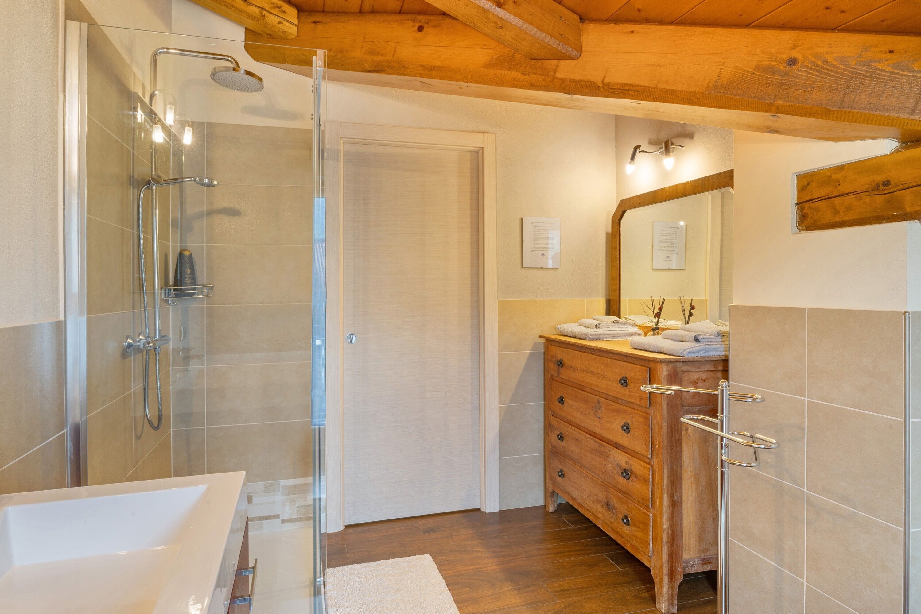 Une salle de bain avec une douche à parois de verre, un meuble-lavabo en bois avec un miroir et une baignoire blanche.