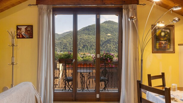 A room with a wooden ceiling, a balcony with chairs and a table, and a view of a mountain.