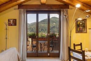 Una habitación con techo de madera, un balcón con sillas y una mesa, y vista a la montaña.