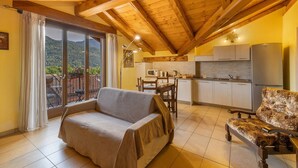 A cozy room with a sofa, a patterned armchair, a dining table, and a kitchen area.