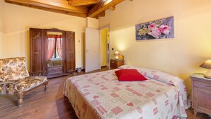 A bedroom with a wooden ceiling, a bed with a patterned bedspread, a bench, a door, and a wall-mounted lamp.