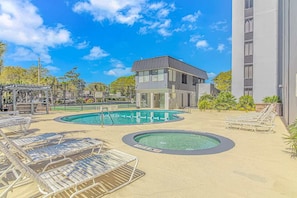 Un área de piscina con varias piscinas, sillones de descanso y un edificio de diseño moderno.