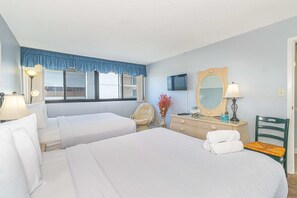 A hotel room with two beds, a television, a mirror, a dresser, and a chair.