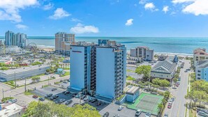 Un hotel di grandi dimensioni con numerosi piani, un parcheggio e vista sulla spiaggia e sull'oceano.