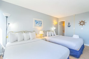 Une chambre double avec deux lits, une table de chevet avec une lampe, un tableau encadré, une ancre fixée au mur et un décor représentant un gouvernail de navire.