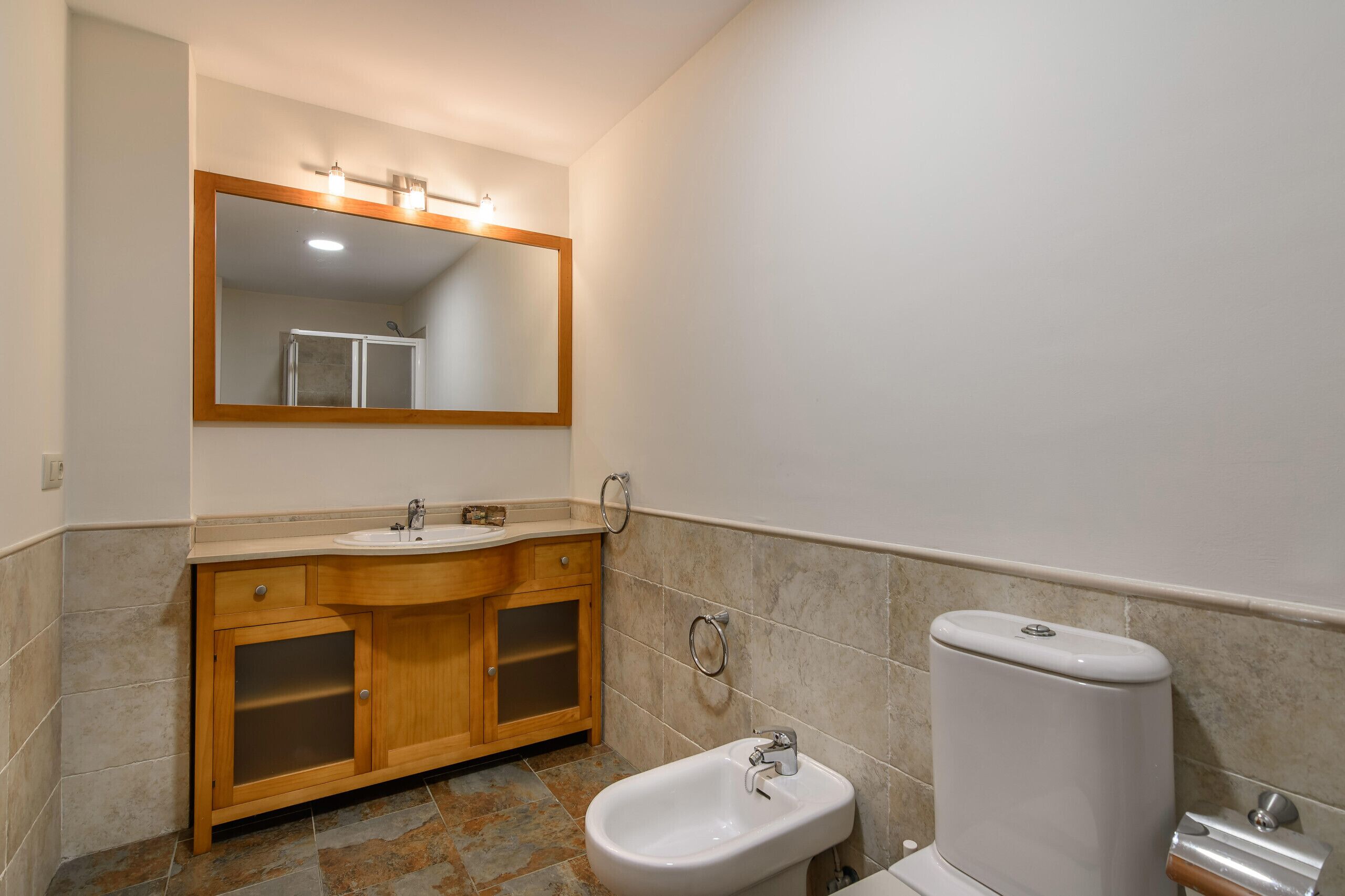 A bathroom with a wooden vanity, a sink, a bidet, and a toilet.
