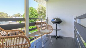 Ein Balkon mit Korbstühlen, einem Grill und Blick auf Bäume und Häuser.