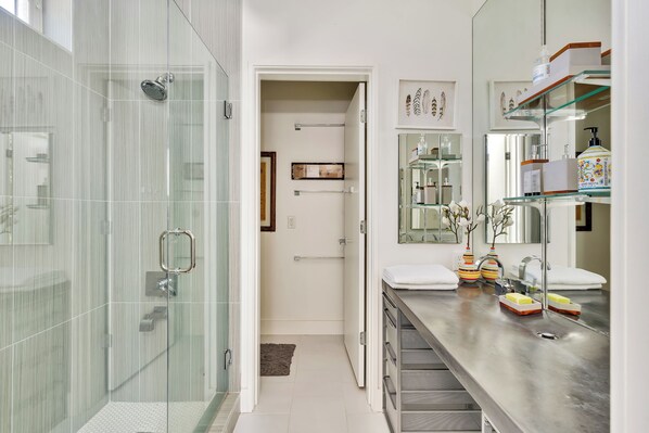 A modern bathroom with a glass shower enclosure, a vanity with a mirror, and a shelf with toiletries.