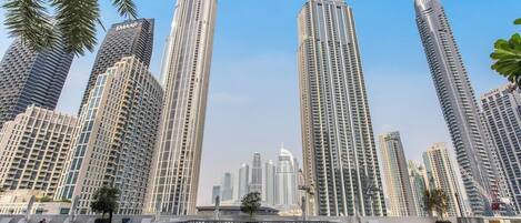 A high-rise building complex with multiple skyscrapers, a rooftop pool area with lounge chairs, and palm trees in the foreground.