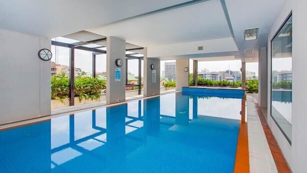 A modern indoor swimming pool with clear glass walls, allowing views of the surrounding buildings and greenery. - Republic Apartment (Spring Hill)