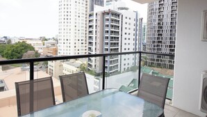 A balcony with a glass table and chairs, overlooking a cityscape with high-rise buildings. - Republic Apartment (Spring Hill)