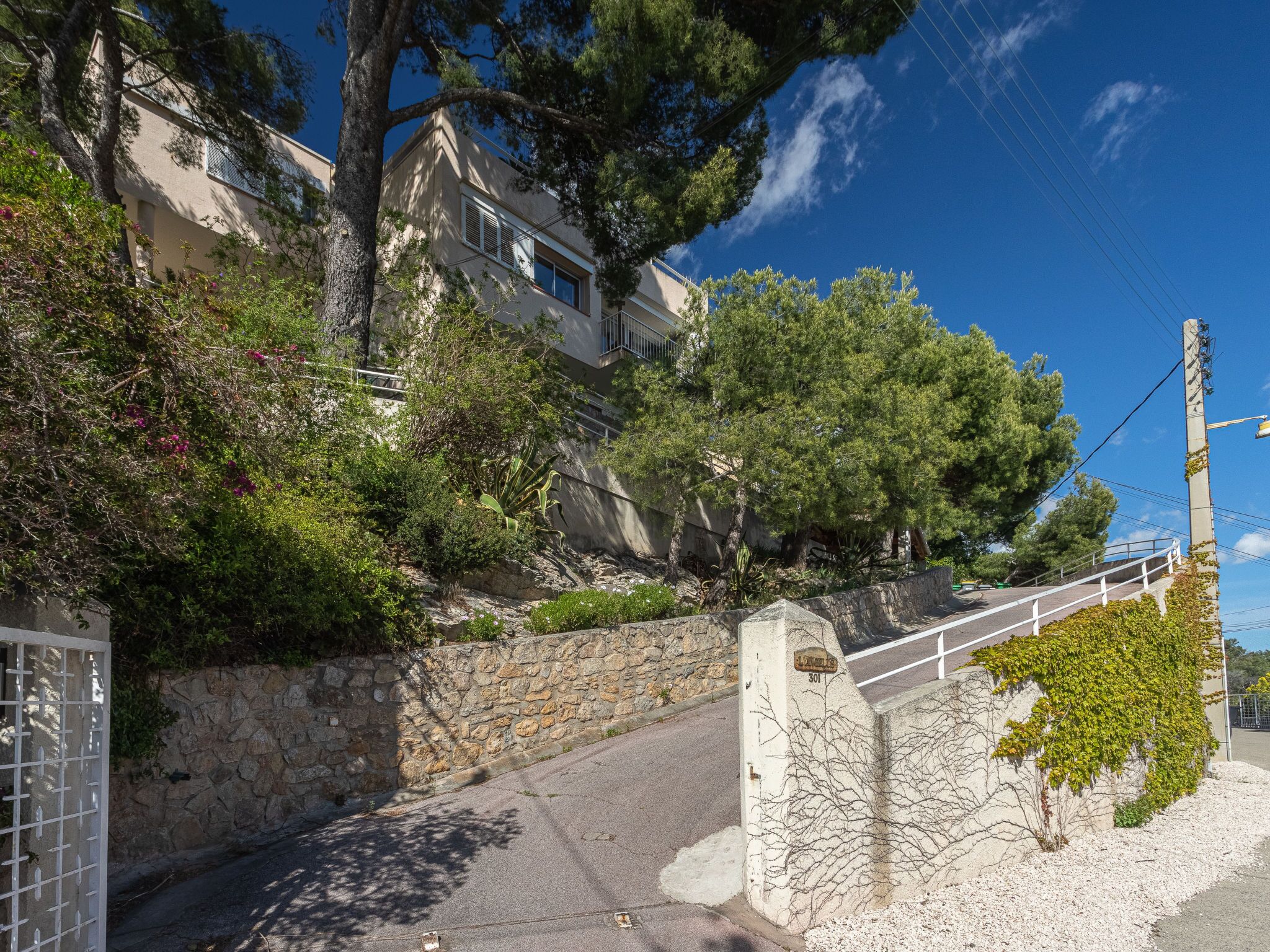 Une ruelle bordée d’un mur de pierre et d’un portail, qui mène à un bâtiment à la façade en pierre sur lequel on peut lire l’inscription « 301 ».