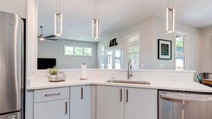 Une cuisine moderne avec des armoires blanches, des appareils en acier inoxydable et des luminaires suspendus.