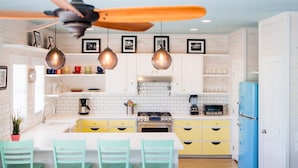 Une cuisine avec des meubles blancs, un réfrigérateur bleu, une cuisinière et un ventilateur de plafond.
