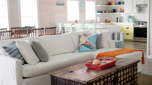 Un salon moderne avec un canapé blanc, une table basse en bois et une cuisine en arrière-plan.