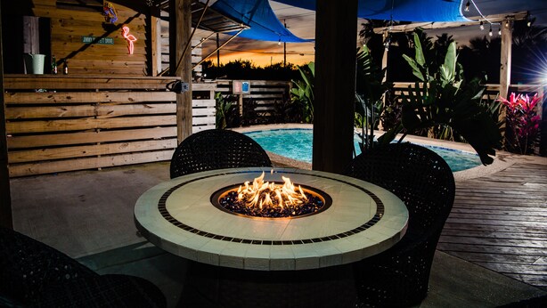 Un espace extérieur aménagé en terrasse, avec un foyer circulaire, une plateforme en bois et une piscine en arrière-plan.
