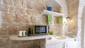 A kitchen with a stone wall, a microwave, a sink, and a shelf with items.