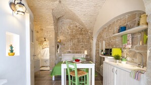 A stone-walled kitchen with a dining table, chairs, and a sink.