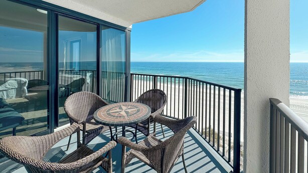 A balcony with wicker furniture and a glass door overlooking the ocean. - BROADMOOR 504 - BEACHFRONT RELAXATION! (Orange Beach)