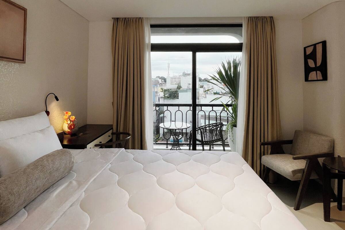 Une chambre d’hôtel avec un grand lit, un bureau avec une lampe, une chaise et un balcon donnant sur la ville.