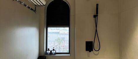 A bathroom with a shower, a toilet, a towel rack, and a window with a view of buildings.