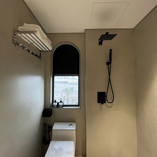 A bathroom with a shower, a toilet, a towel rack, and a window with a view of buildings.