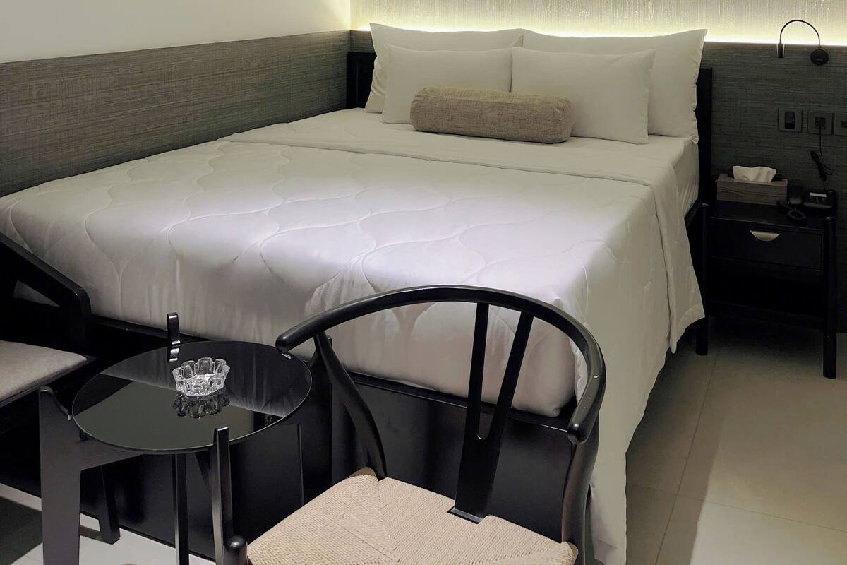 Une chambre d’hôtel comprenant un lit, une table de chevet, une chaise et une lampe fixée au mur.